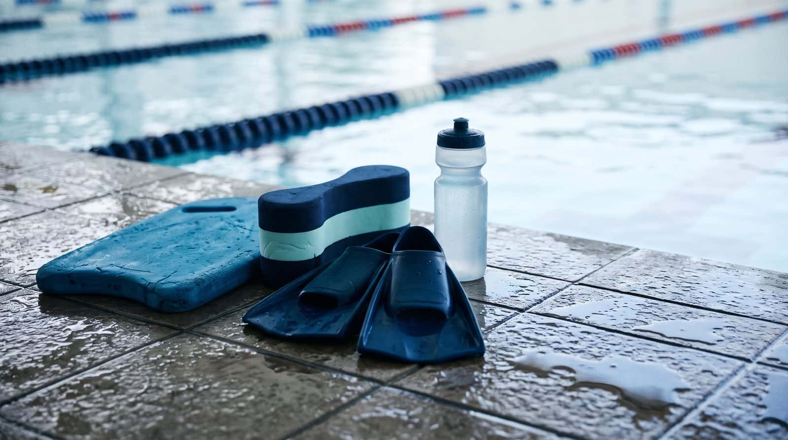 Kickboard, pull buoy, fins and a water bottle on the pool deck