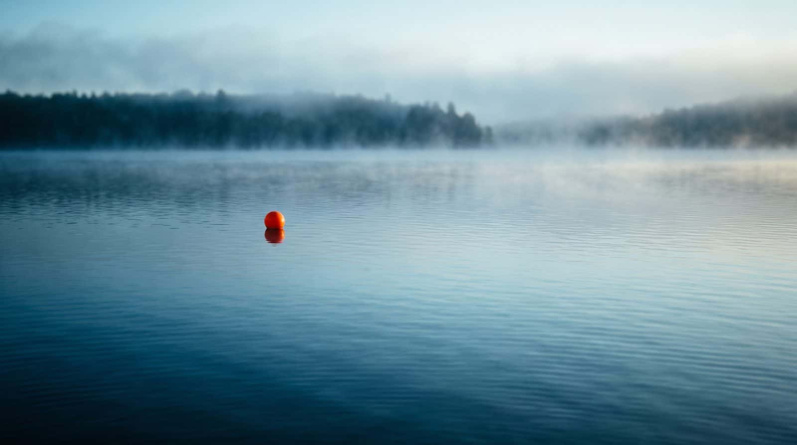Orange buoy on calm open water in morning mist
